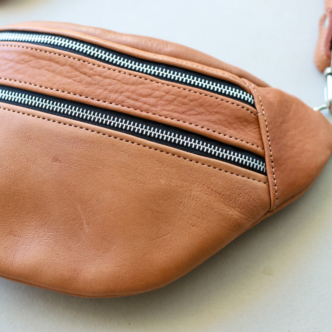 Brown leather fanny pack with a zipper on a light background
