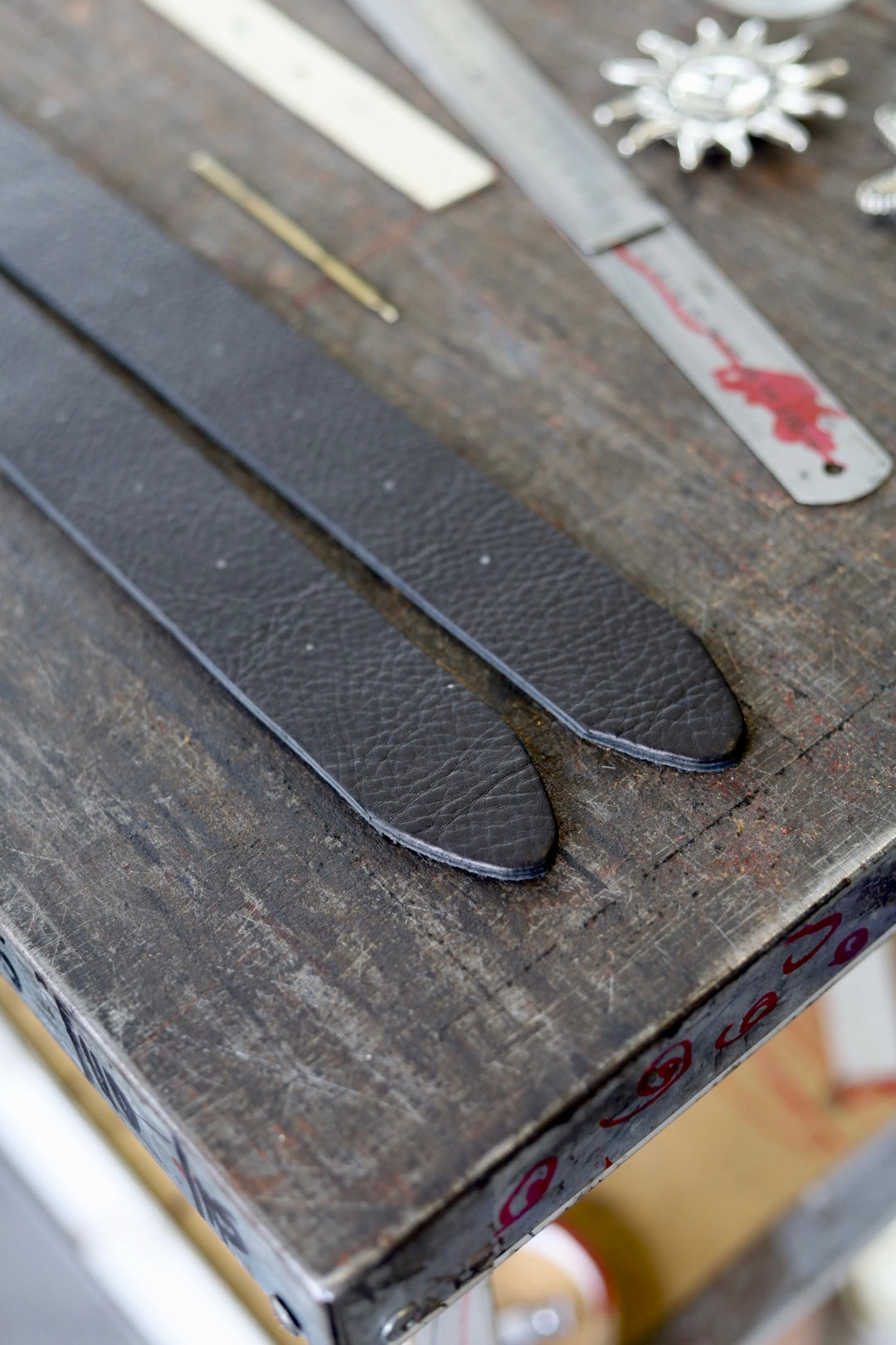 Two black leather straps on a wooden surface with tools in the background