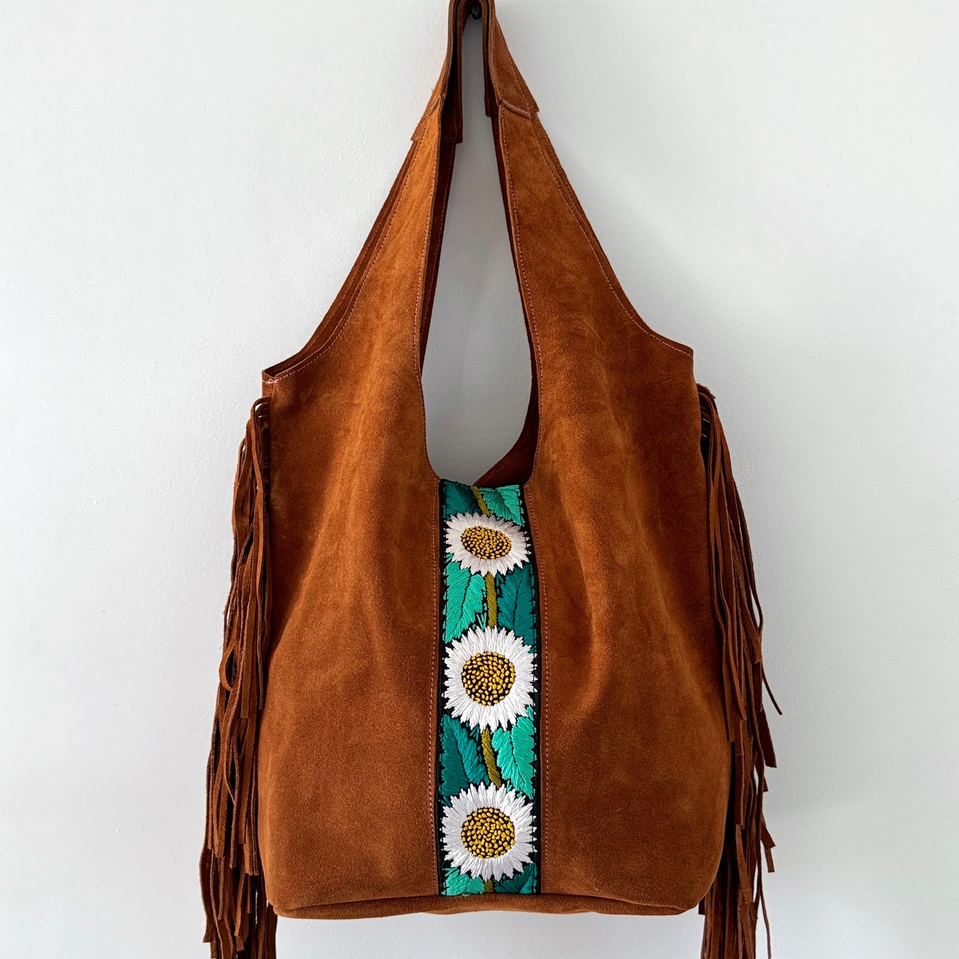 Brown suede handbag with floral embroidery and fringe on a white background