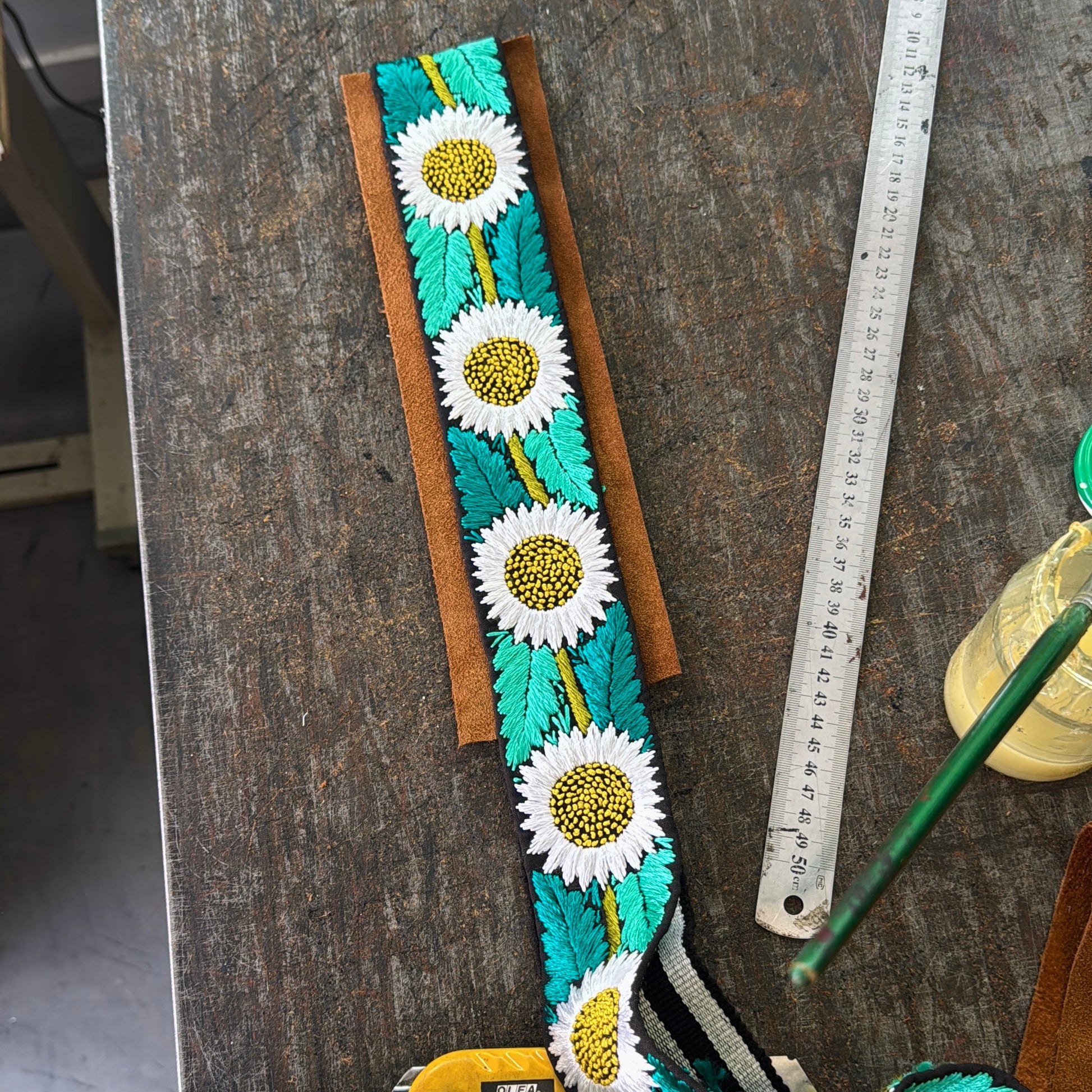 Decorative belt with floral patterns on a wooden surface with tools.