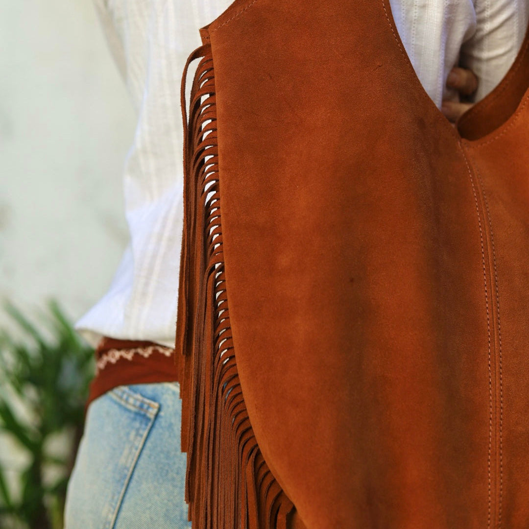 Brown leather vest with fringe over a white shirt and jeans, blurred background
