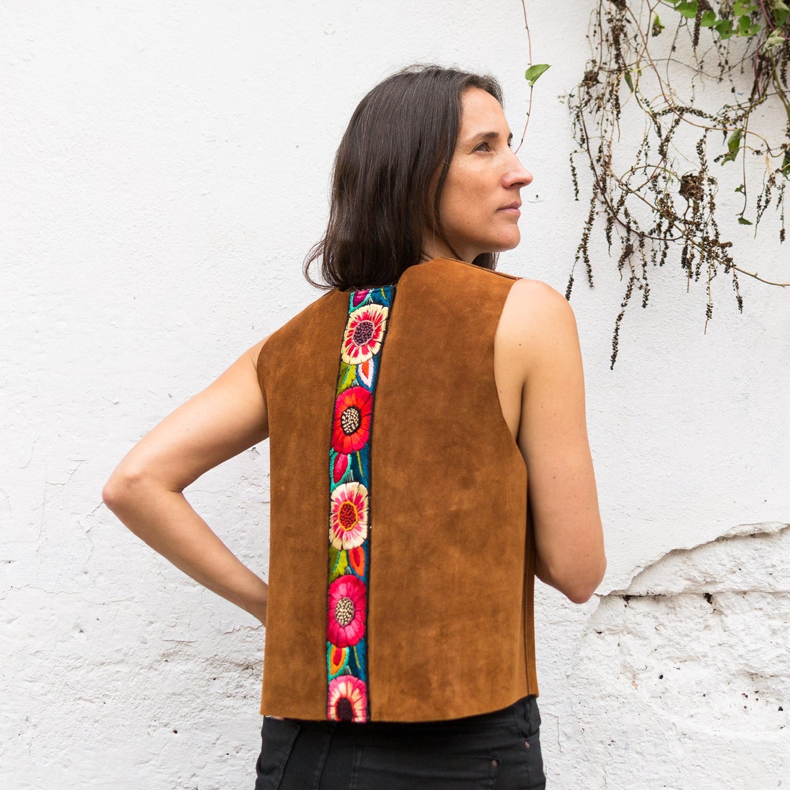 Woman wearing a brown vest with floral embroidery on a white wall background