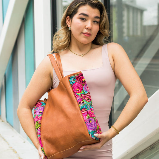 Woman holding a brown leather handbag with floral pattern, standing outdoors.