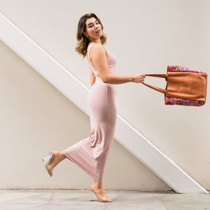 Woman in a pink dress holding a brown leather bag with floral pattern on a staircase.