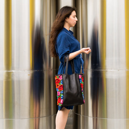 Woman holding a floral tote bag against a metallic wall.