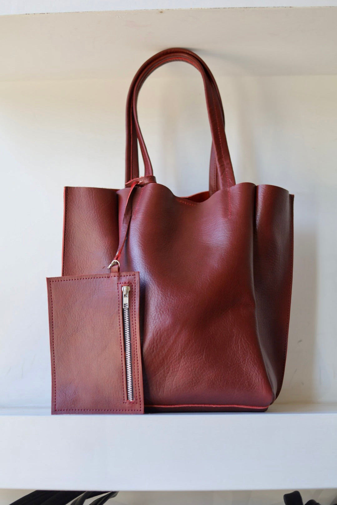 Brown leather tote bag with a front pocket on a white surface