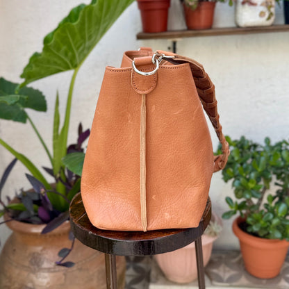 Tan leather backpack on a small round table with plants in the background