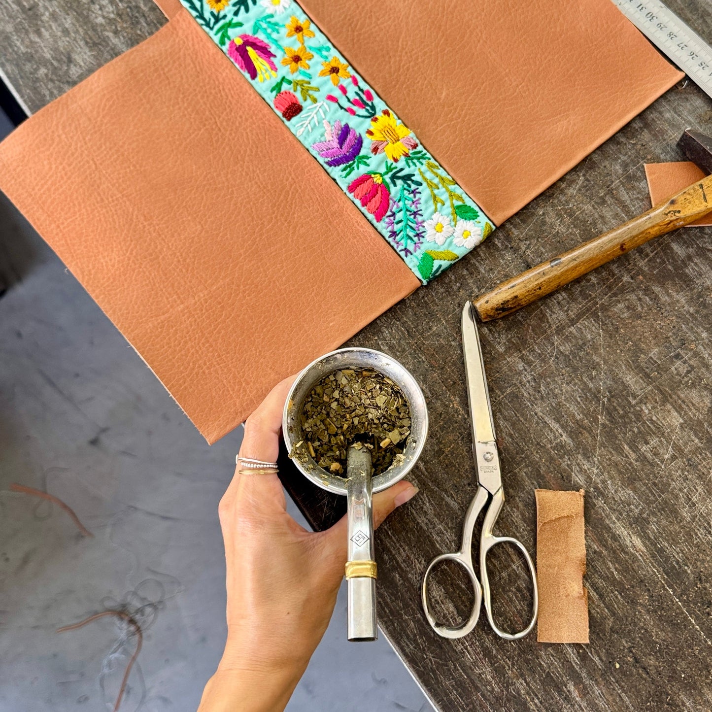 Hand holding a small container of herbs on a wooden surface with tools and materials.
