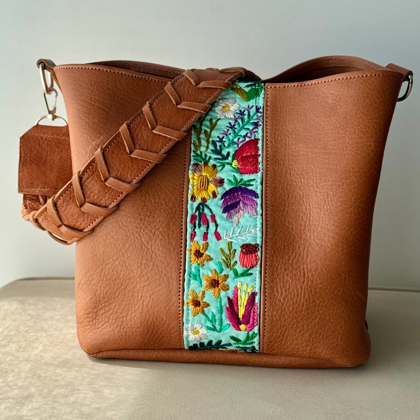 Brown leather handbag with a floral strap on a neutral background