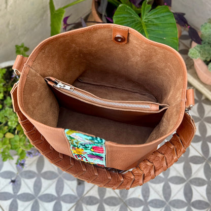 Brown leather bag with a colorful label on a patterned floor with plants in the background