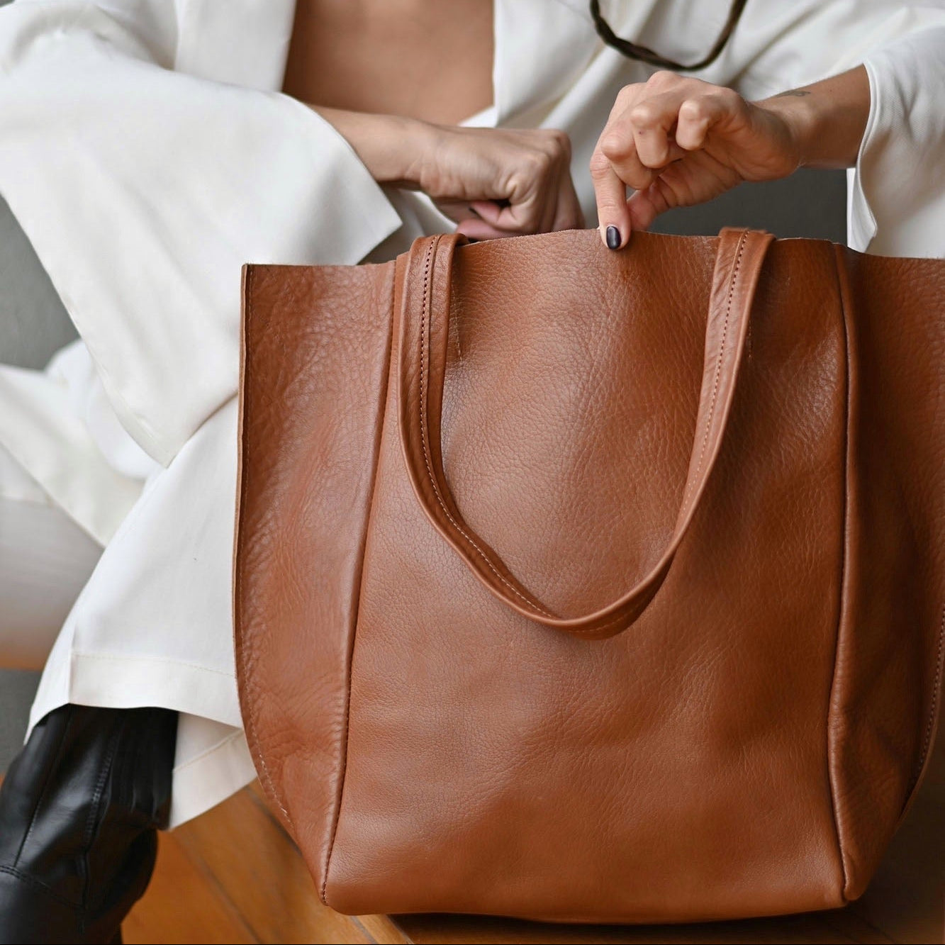 Woman in a white coat opening a brown leather tote bag.