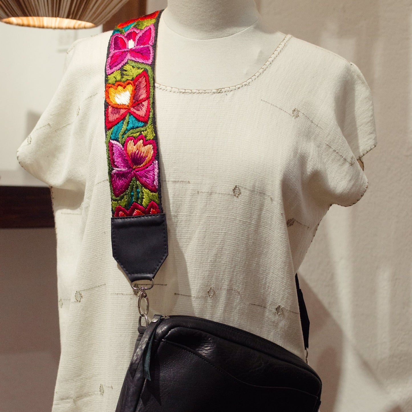 Black bag with a colorful strap on a mannequin against a neutral background