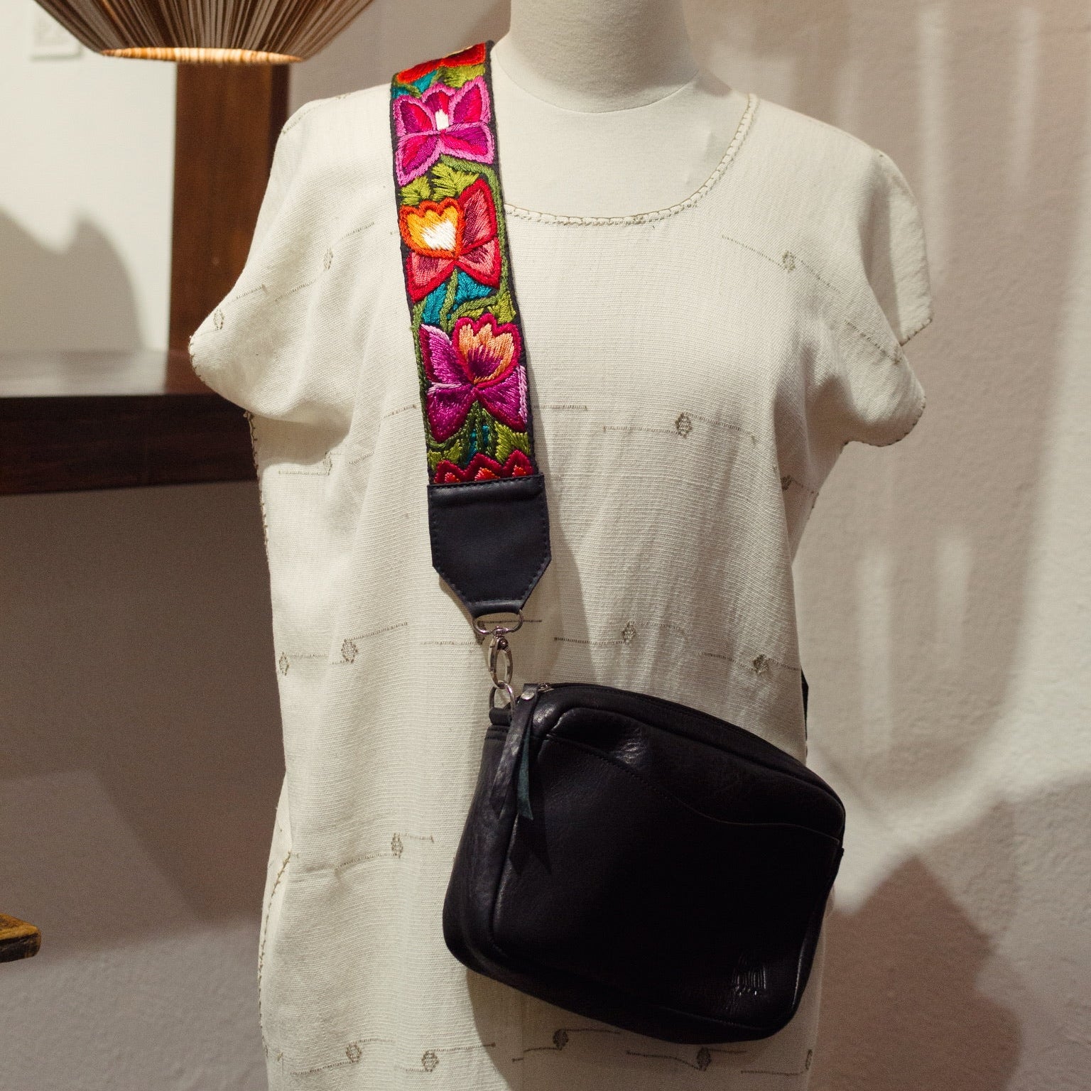 Mannequin wearing a white dress with a black bag and colorful strap in a room setting.