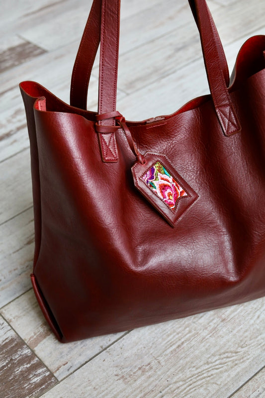 Brown leather handbag with a colorful tag on a wooden floor