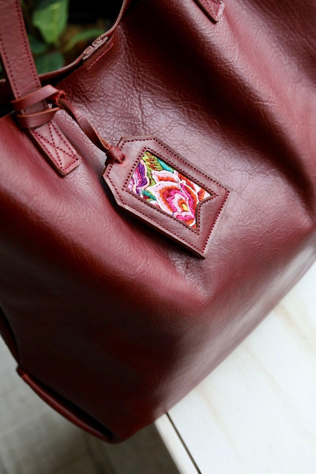 Brown leather bag with a decorative tag featuring a colorful rose design.