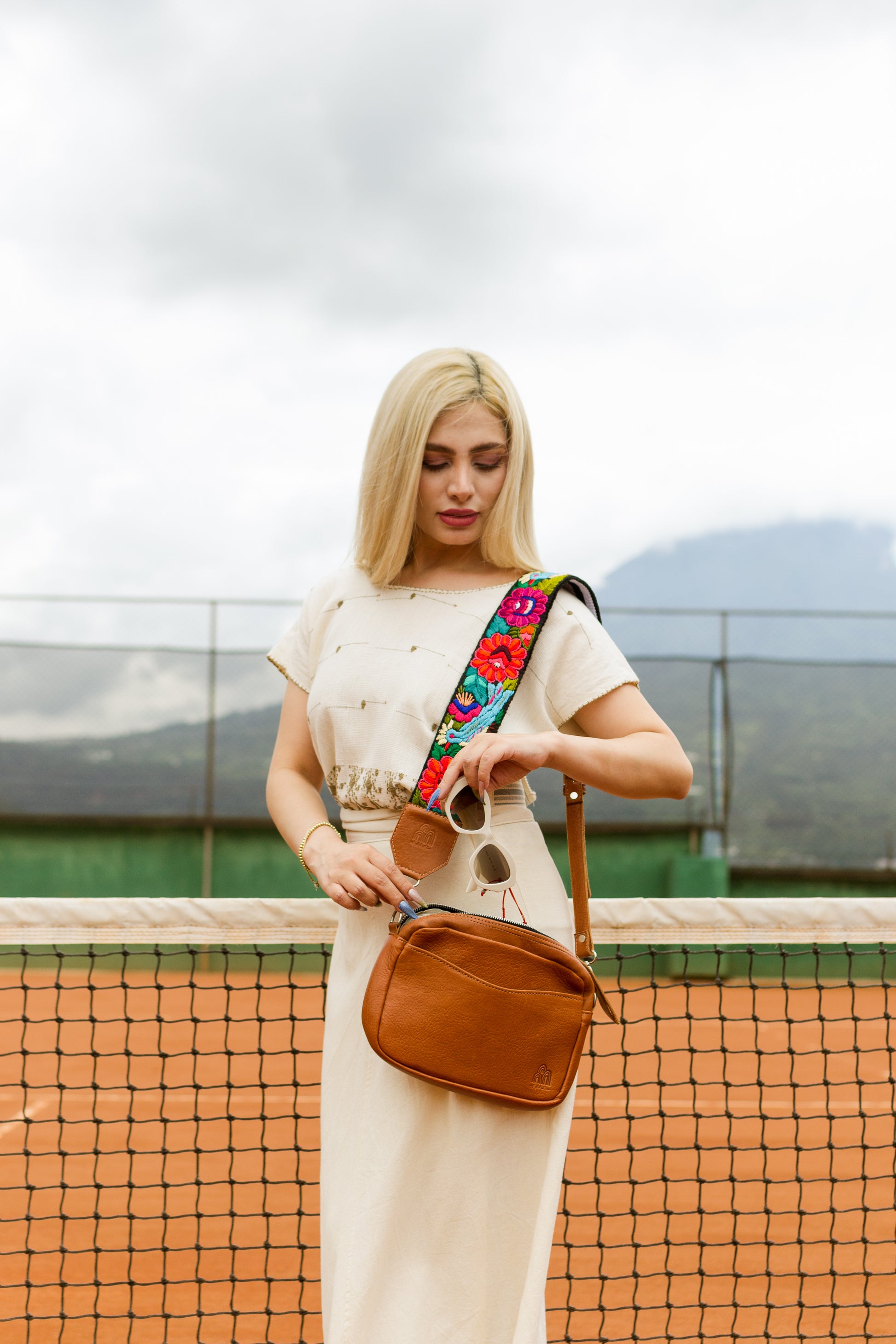 Woman holding a brown bag with a colorful strap on a tennis court