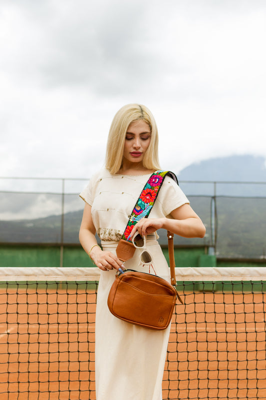 Woman holding a brown bag with a colorful strap on a tennis court