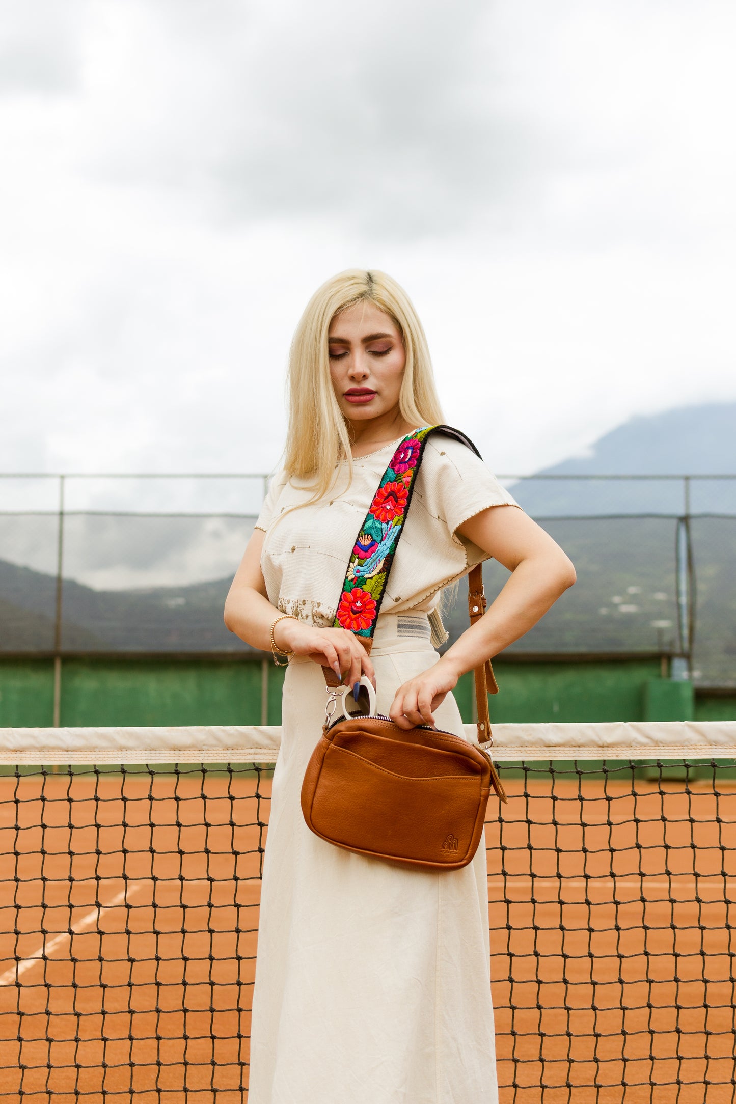 Woman holding a brown bag on a tennis court with mountains in the background