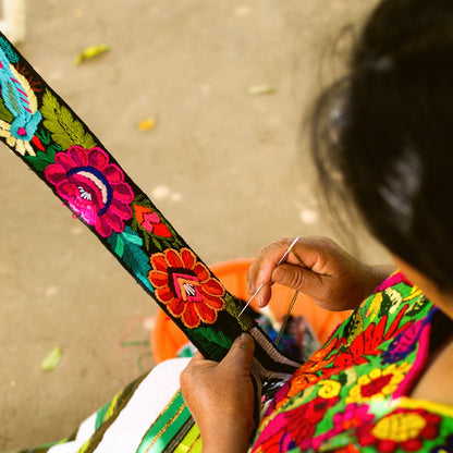Person wearing a colorful embroidered garment with a close-up of their hand holding a needle and thread.