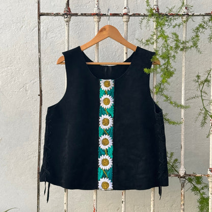 Black sleeveless top with sunflower pattern on a wooden hanger against a white wooden fence.