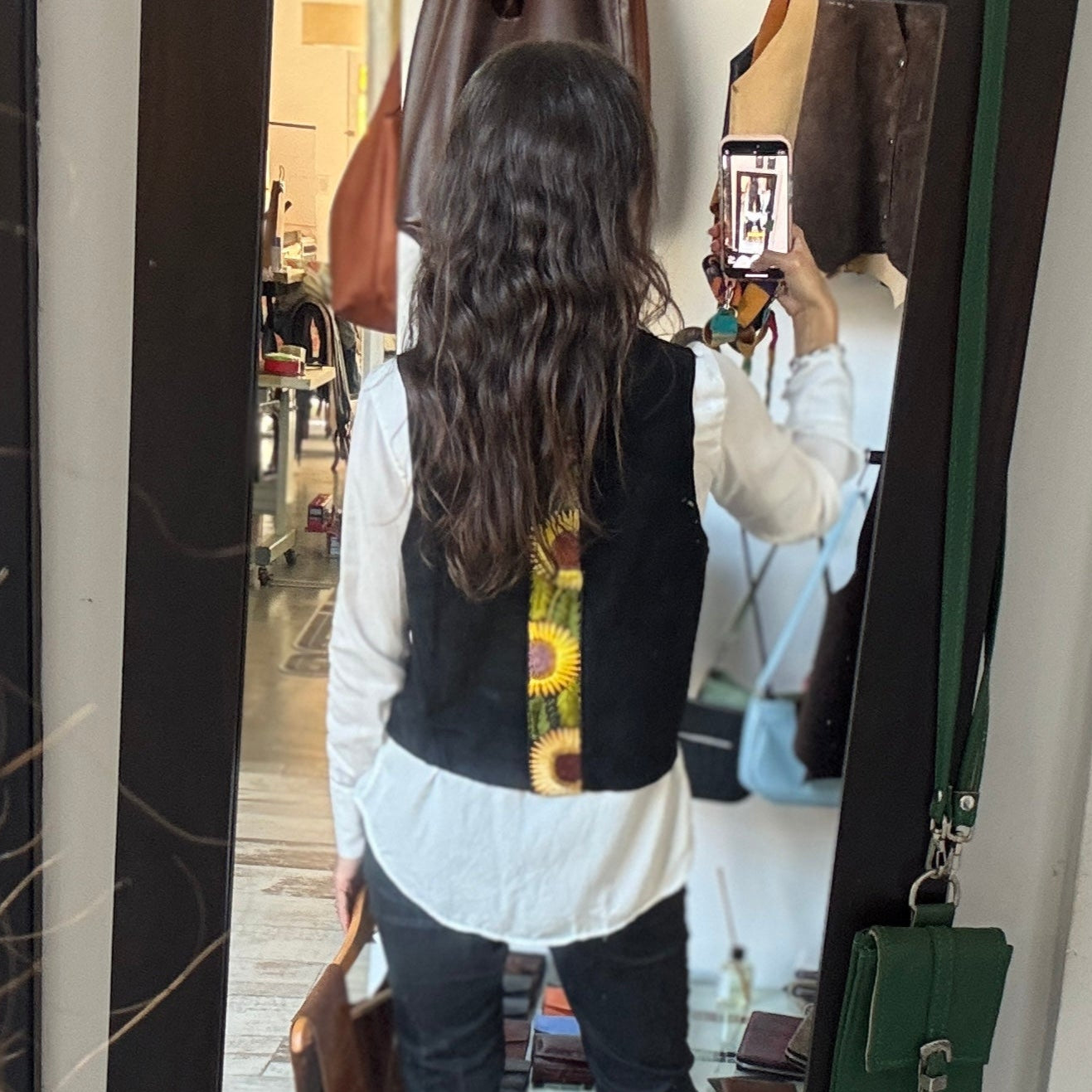 Person looking at themselves in a mirror wearing a white shirt, black vest, and dark pants.