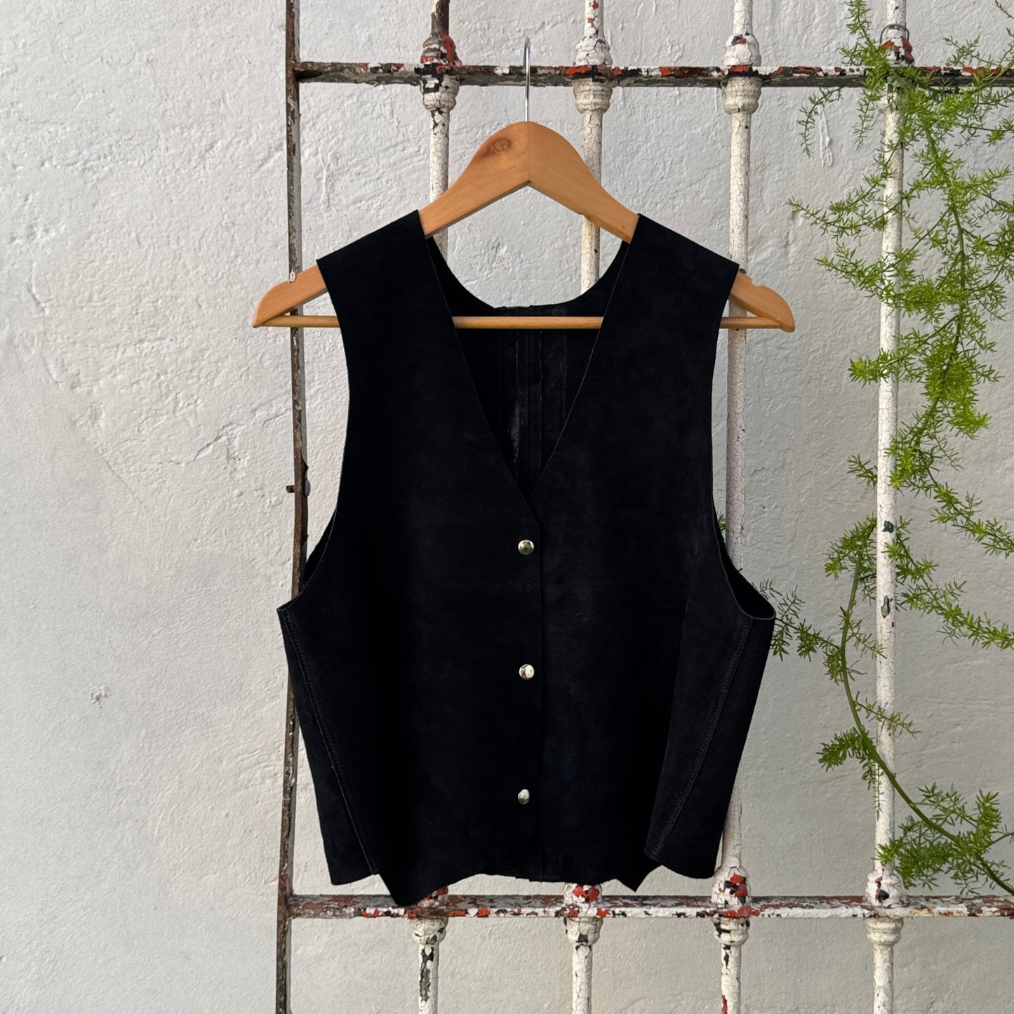 Black sleeveless top on a hanger against a white wooden panel background with greenery.