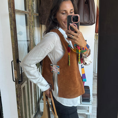 Person wearing a brown vest with decorative elements, standing in front of a mirror.