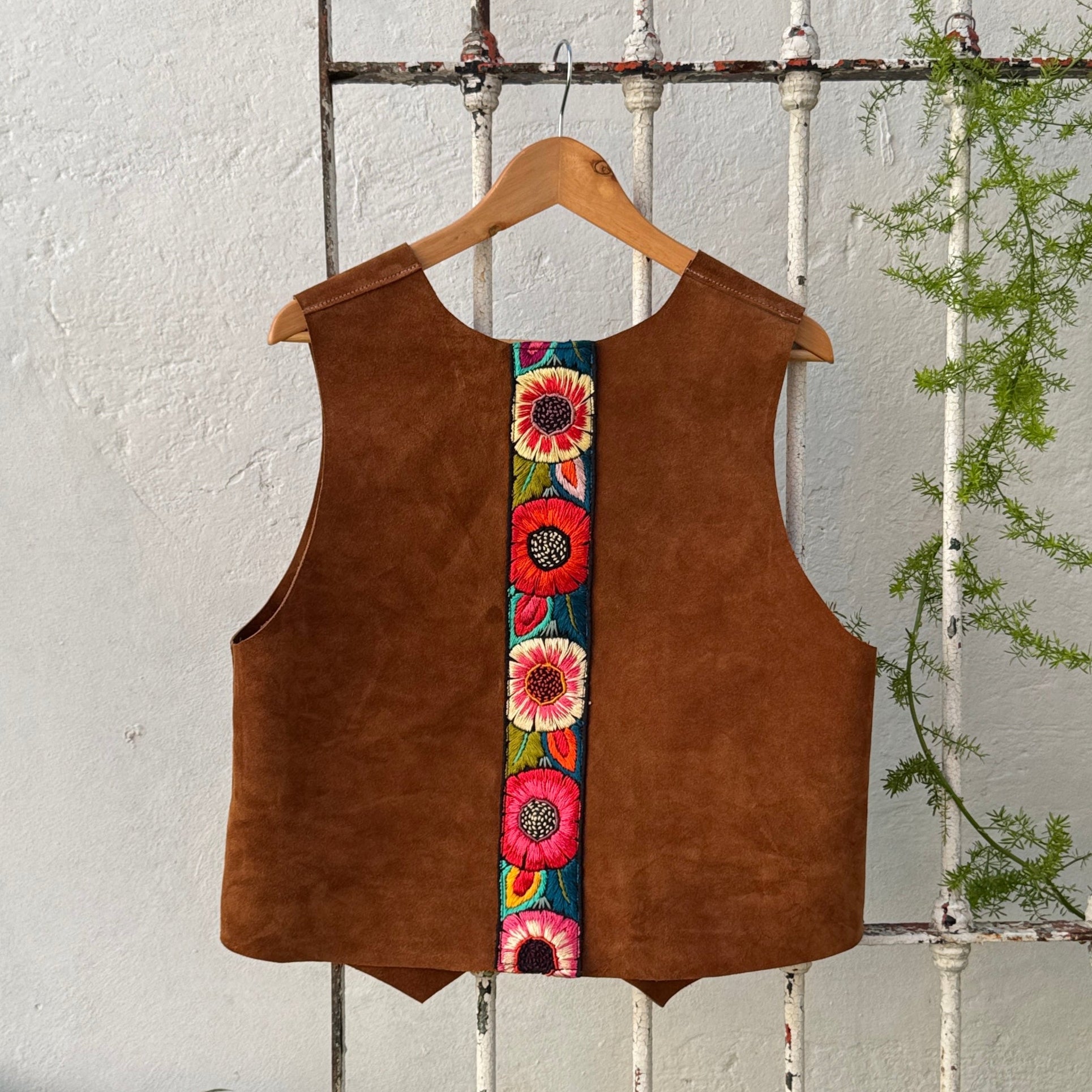 Brown vest with colorful floral pattern on a hanger against a white wooden fence.