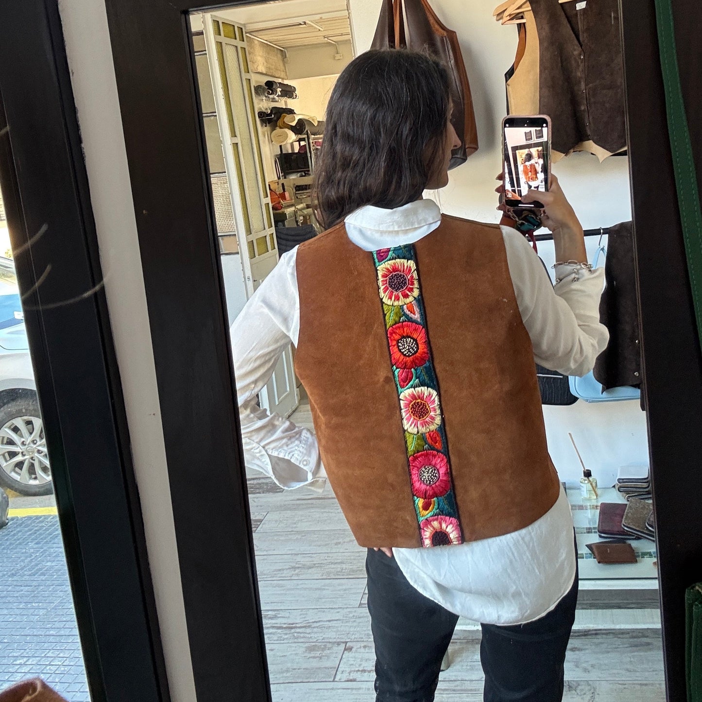 Person wearing a brown vest with floral patterns taking a mirror selfie.