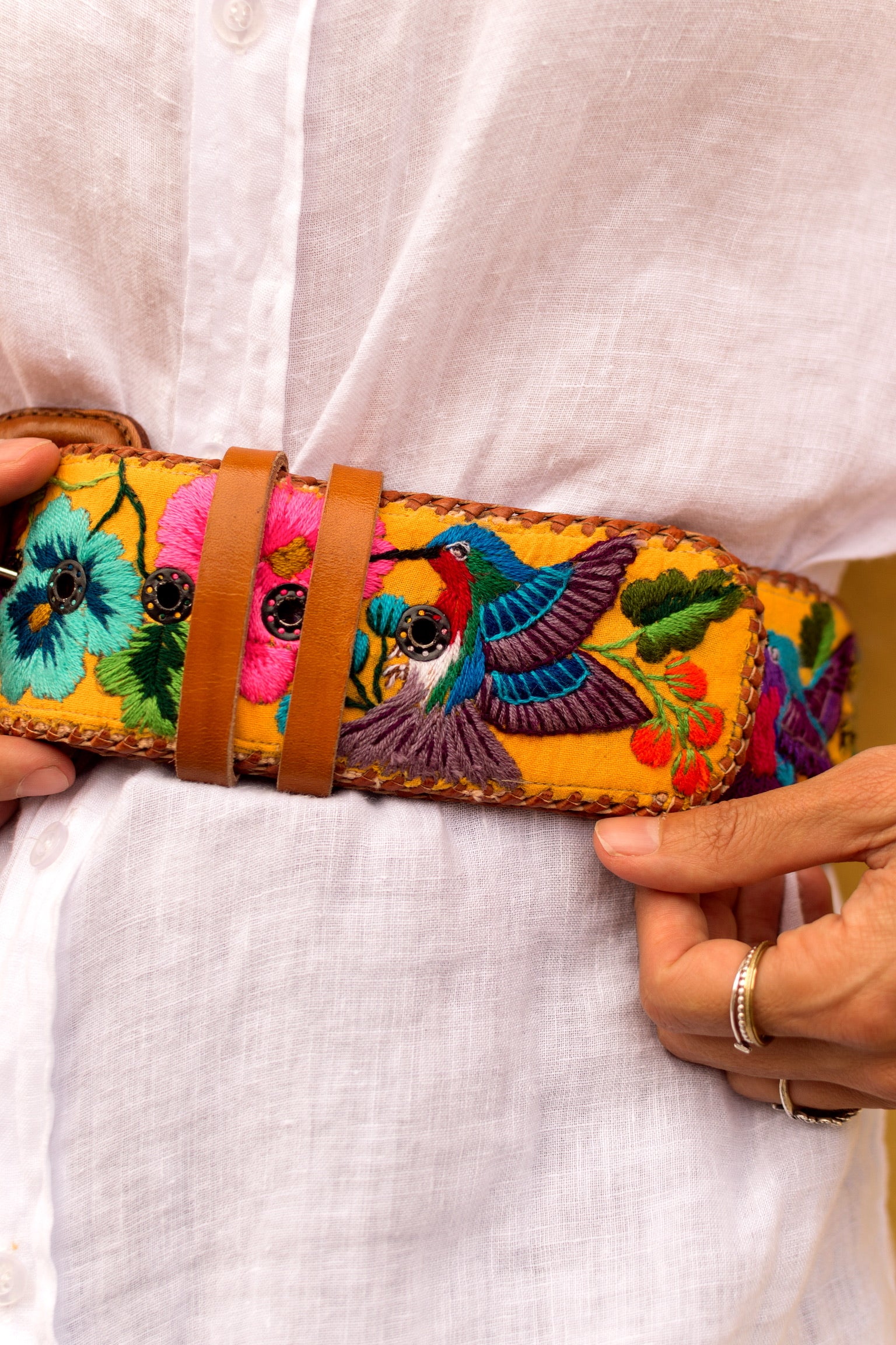 Colorful embroidered belt with birds and flowers held by a person wearing a white shirt.