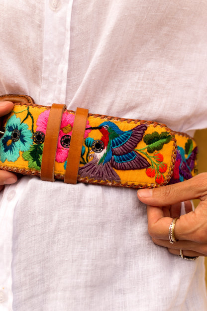 Colorful embroidered belt with birds and flowers held by a person wearing a white shirt.
