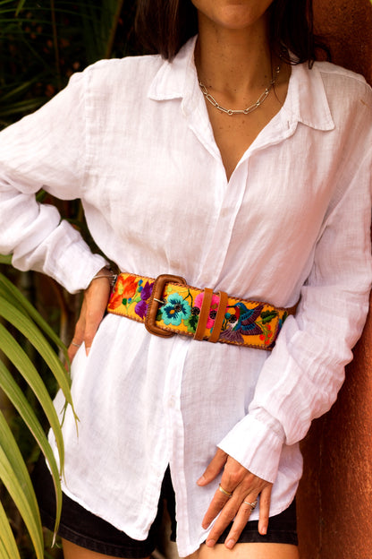 Person wearing a white shirt and colorful belt with a plant in the background