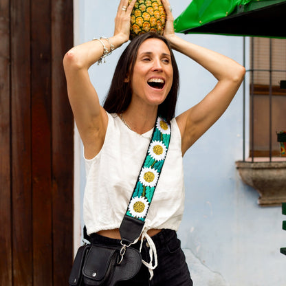 Woman holding a pineapple on her head with a colorful bag strap over her shoulder, standing in front of a building with a green awning.