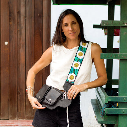 Woman holding a black bag with a colorful strap in front of a green structure.