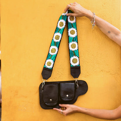 Black leather bag with a colorful floral strap against a yellow wall