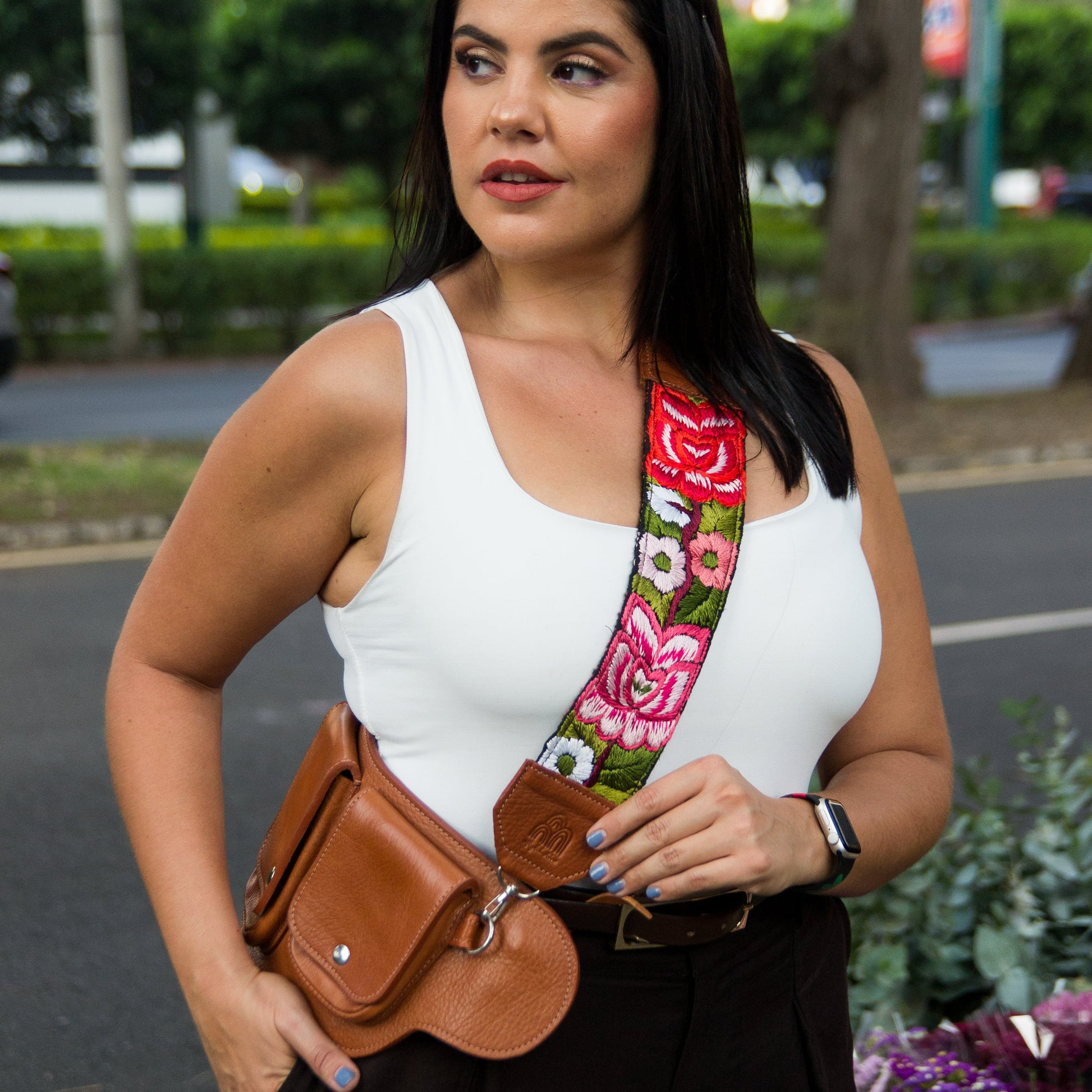 Woman wearing a white top and brown leather bag with a colorful strap in an outdoor setting.
