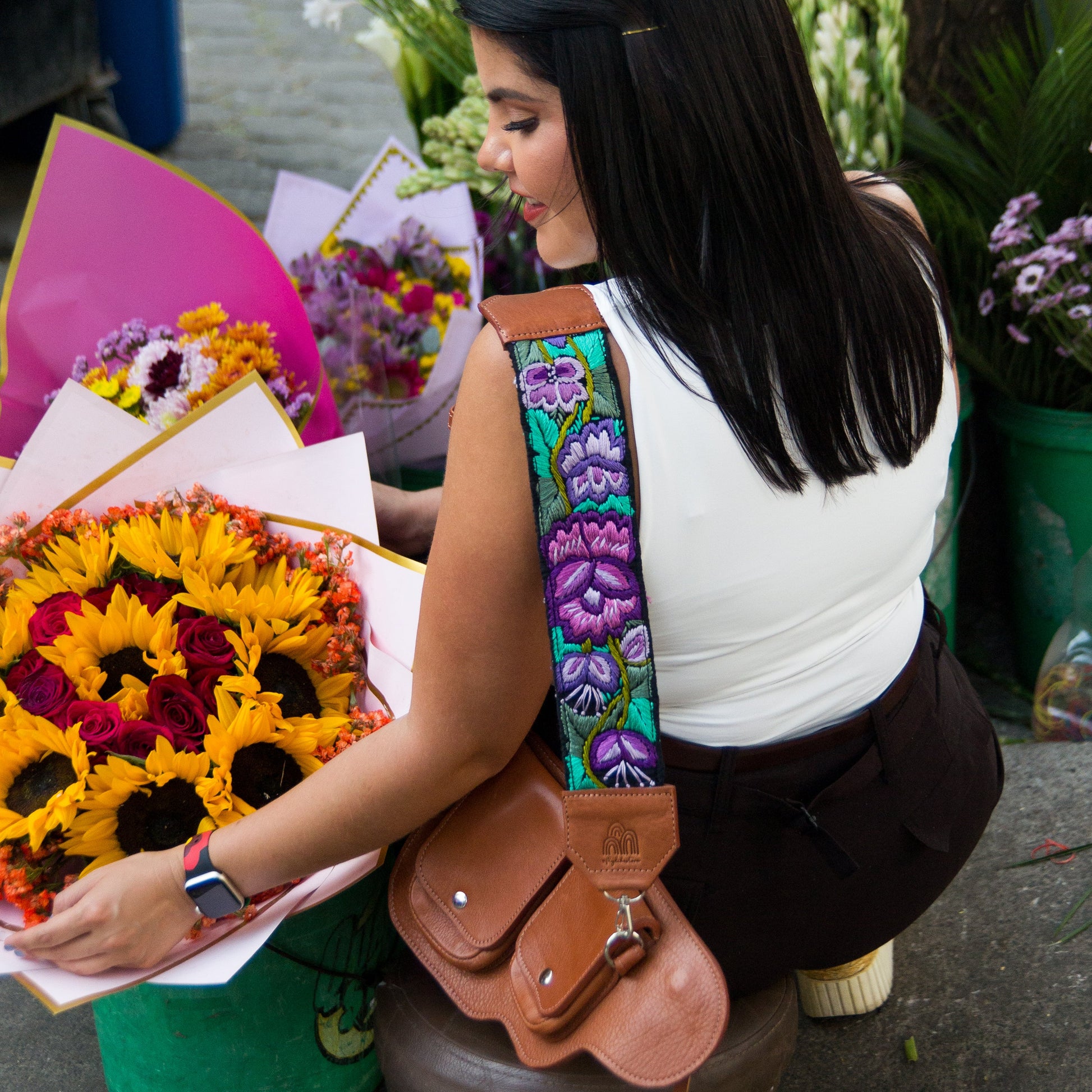 Woman arranging flowers at a market stall with colorful flowers and a floral-patterned bag.
