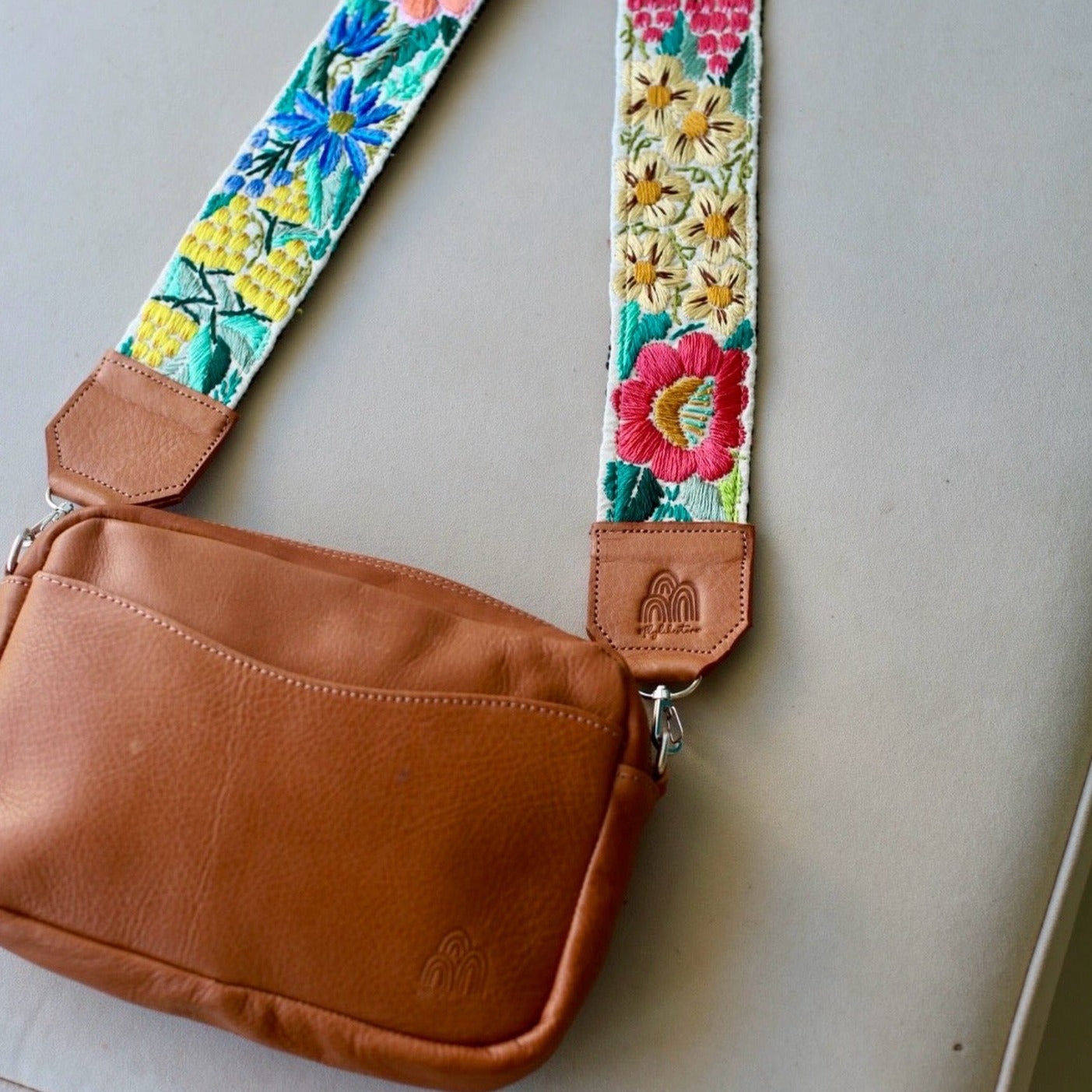 A brown travel strap with a floral pattern and a leather buckle, displayed on a flat surface.