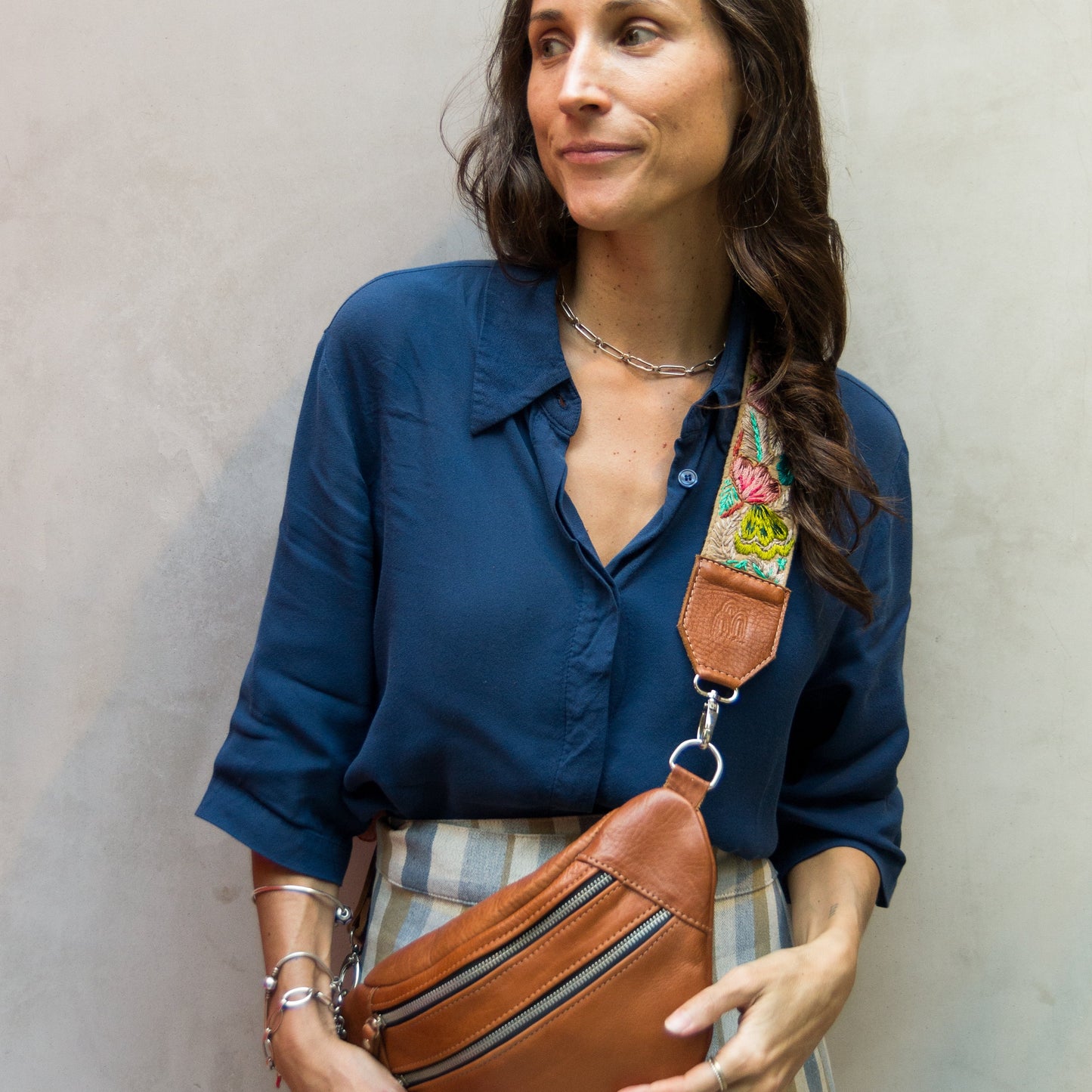 Woman holding a brown leather waist bag against a plain background