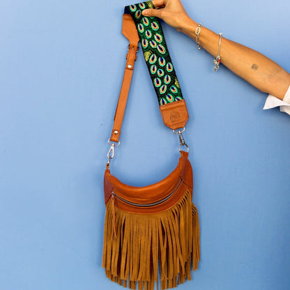 Brown leather handbag with peacock feather strap against a blue background