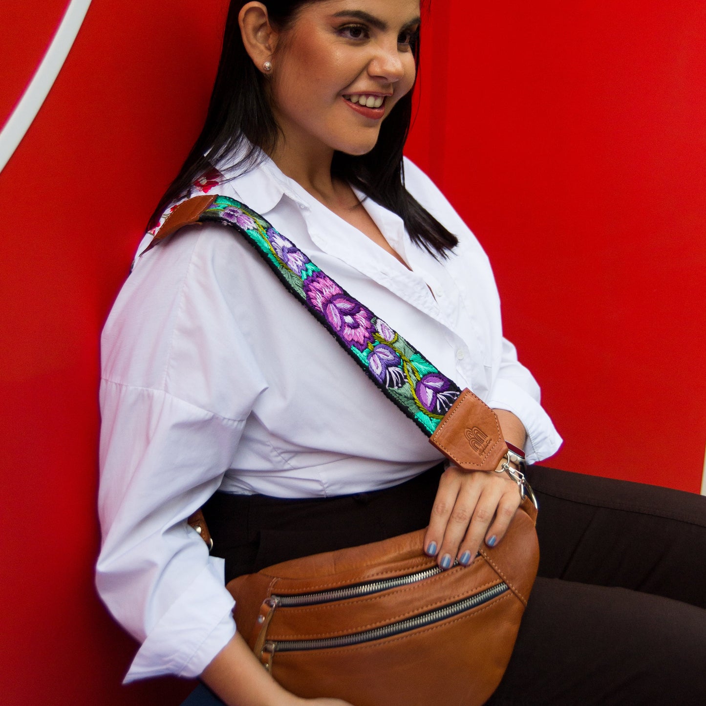 Woman holding a brown leather bag with a colorful strap against a red background