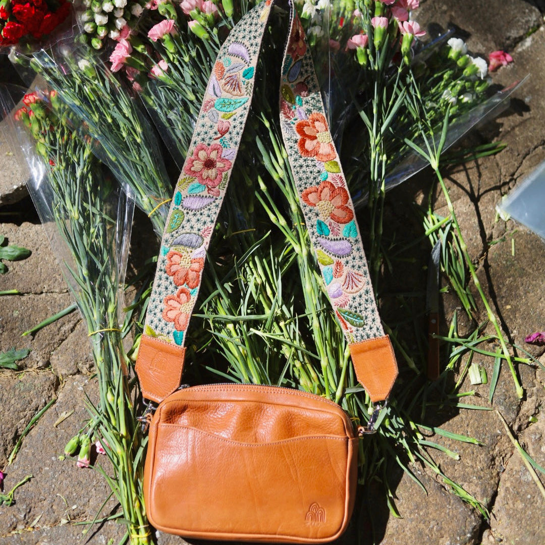 Brown leather bag with a colorful strap on a bed of flowers and leaves.